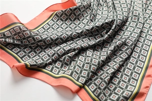 Gros plan d'un foulard en soie géométrique avec motif à carreaux et bordure corail