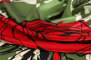 Detailed close-up of glossy red and green floral print on smooth silk-like fabric scarf