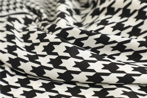 Detailed close-up of glossy black and white houndstooth pattern fabric with elegant folds