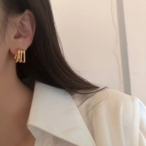 Close-up of triple-layered gold geometric rectangular stud earrings worn on a model's ear