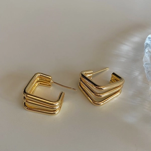 Close-up of geometric triple-layered square gold earrings on a minimalist background