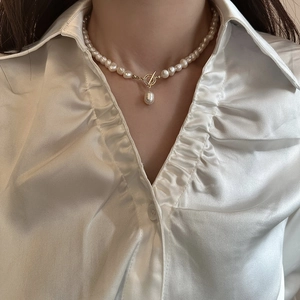 Détail du collier de perles d'eau douce avec fermoir OT doré sur chemise en soie