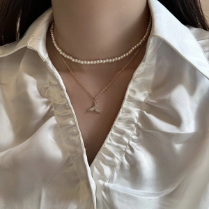 Close-up of double-layered pearl choker and gold fish tail pendant necklace on model