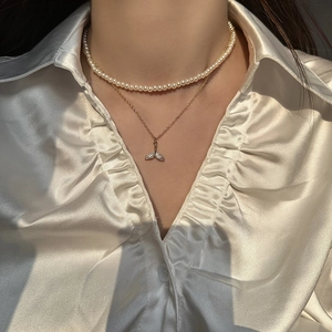 Close-up of double-layered pearl necklace with crystal fishtail pendant on silk shirt