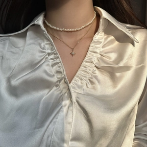 Detail of double-layer necklace with small pearls and gold starburst pendant on model