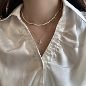 Close-up of double-layer pearl necklace with a micro-set floral pendant on white satin