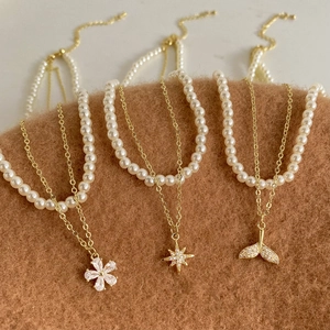 Double-layered pearl necklace set with gold floral and star pendants on a warm felt background