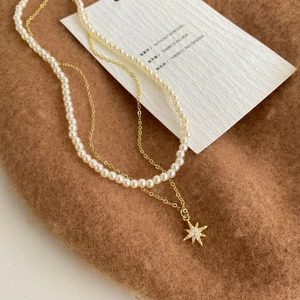 Detail of double-layer pearl necklace featuring a gold star pendant with micro-inlaid stones