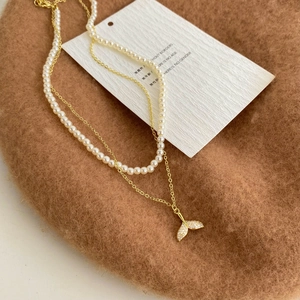 Detail of double-layer pearl necklace with gold fish tail pendant and zircon stones