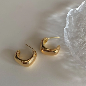 Detailed macro view of polished gold C-shape geometric earrings on a textured glass surface