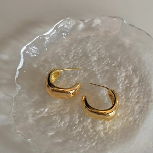 Macro shot of minimalist gold geometric U-shaped hoop earrings on frosted glass