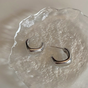 Detailed view of silver C-shaped geometric earrings on a textured glass plate