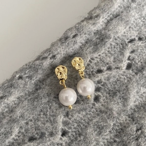 Vue détaillée de boucles d'oreilles perles avec base dorée sur tissu en maille grise
