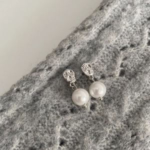 Détail de la boucle d'oreille texture argentée et perle ronde sur tricot gris