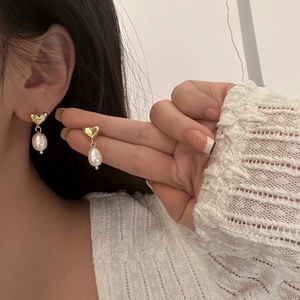 Close-up of golden heart earrings with teardrop pearls on a model wearing lace