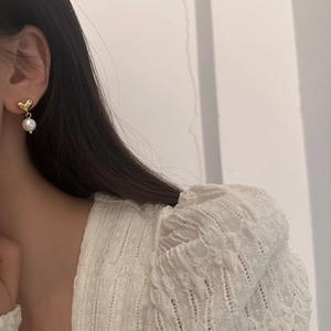 Elegant gold heart earrings with white freshwater pearls shown on a female model