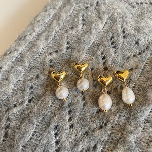 Elegant gold heart earrings with freshwater pearls on grey knit fabric background