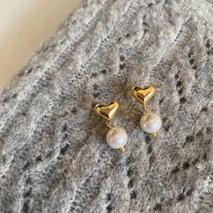 Detail of gold heart earrings with white freshwater pearls on a grey knit background
