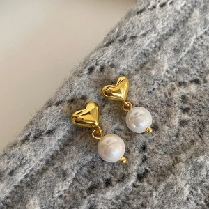 Detail of golden heart stud earrings with white pearls on a grey knit sweater
