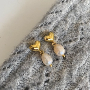 Detail of gold heart earrings with dangling baroque pearls on a knitted fabric backdrop