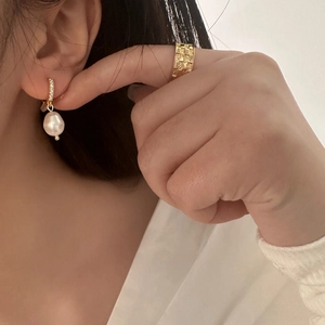 Close-up of gold plated baroque pearl earrings with micro pavé zircon and a checkered ring