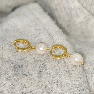 Close-up of gold pearl hoop earrings with zircon pavé on a grey knit sweater background