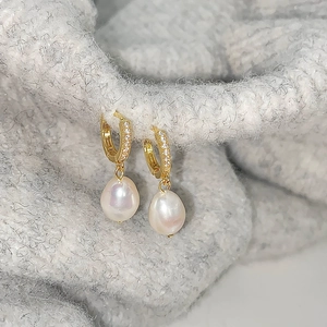 Detail of gold zircon hoop earrings with natural drop-shaped freshwater pearls on knitwear