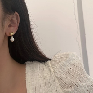 Elegant gold heart stud earrings with white freshwater pearls worn by a model