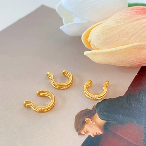 Detailed view of three gold-plated ear cuffs with zircon inlay on a magazine background