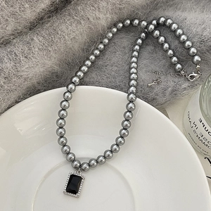 Detailed close-up of a pearl necklace featuring a black gemstone pendant on a white plate
