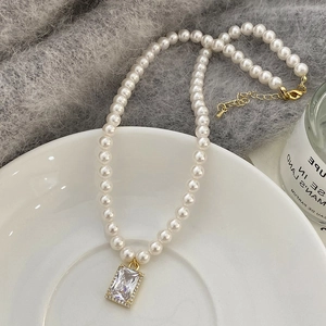 Detail of pearl necklace featuring rectangular zircon pendant on a white ceramic plate