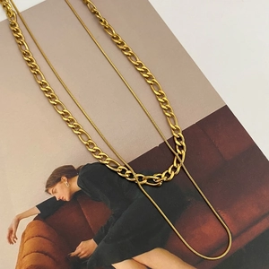 Detail of layered gold double-strand snake and tank chain necklace on a magazine background
