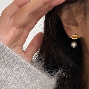 Detail of a knot design earring with a gray pearl drop worn by a model on a dark background