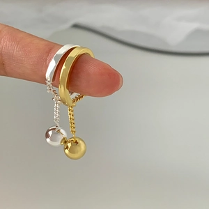 Detail of gold and silver chain drop earrings with spherical charms on a finger