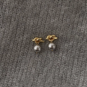 Detail view of gold knot stud earrings with gray pearls on a soft knit background