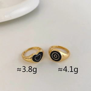 Detail view of gold adjustable open rings with black enamel heart and circular patterns