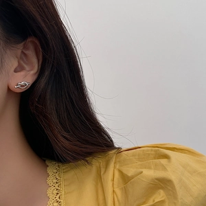 Close-up of minimalist silver knot stud earring worn by model on a grey background
