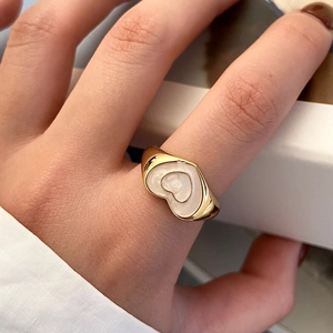 Close-up detail of a vintage golden heart ring with white enamel inlay on a model hand