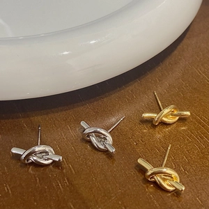 Minimalist knot stud earrings in gold and silver finish on textured wood