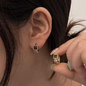 Close-up of golden huggie earrings with emerald zircon and colorful gemstones