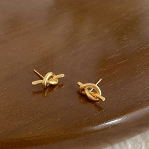 Detailed close-up of gold-plated knot stud earrings on a dark wood background