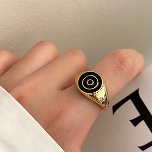 Close-up of a gold-plated heart ring with black enamel concentric circles on a hand