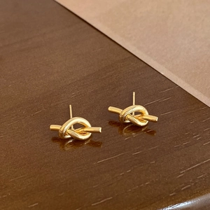 Macro shot of gold-plated knot stud earrings showing smooth texture on wooden surface
