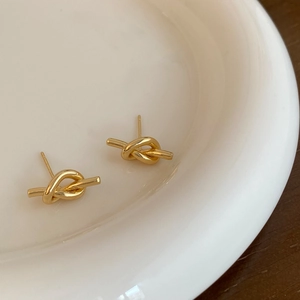 Minimalist gold bow knot stud earrings displayed on a white ceramic tray with wood background