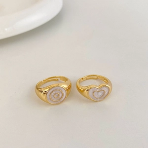 Detailed top view of gold heart and circle rings with white oil drip inlay on light background