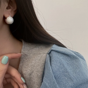 Elegant round mother-of-pearl stud earrings with silver textured frame on model