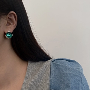 Detail view of a vintage-style earring featuring a green glass stone with a silver border