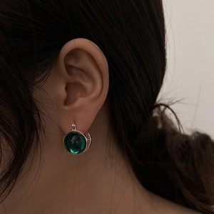 Close-up of vintage emerald green glass earring with intricate beaded metal border detail