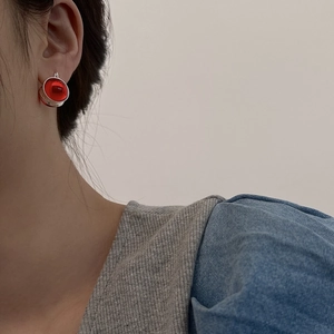 Detail of red globe stud earring with textured silver base worn on model's ear