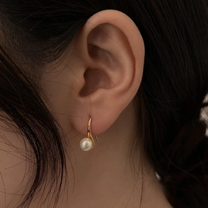 Elegant white pearl drop earrings with gold hooks worn by a model in a close-up shot